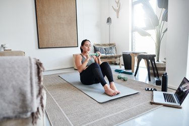 Person in living room performing a crunch with a dumbbell.