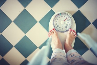 overhead photo of person's feet on bathroom scale on tiled floor