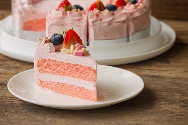 White chocolate strawberry yogurt cake decorated with fresh fruits and chocolate chunk on wood table. Delicious and sweet pink cake for Valentines or birthday party. Homemade bakery concept.