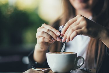 Woman adding sugar to fresh aromatic coffee on table, closeup