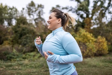 an adult wearing a long sleeve blue athletic top runs outside as an example of calories burned in a workout