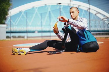 Runner with a shaved head and prosthetic left leg eating a banana, a good snack for track meets