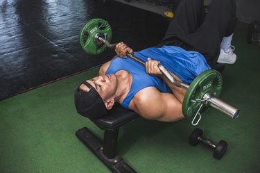 Person in gym working out their chest with an EZ curl bar.