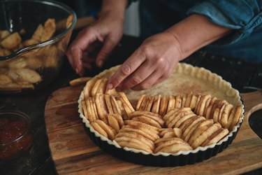 a close up of a person's hand preparing an apple pie on a wooden cutting board at home