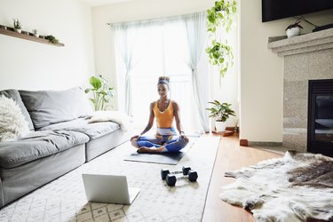 Woman resting in lotus position during virtual workout in living room