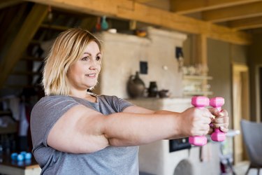 person lifting pink dumbbells to tone "flabby" arms in basement