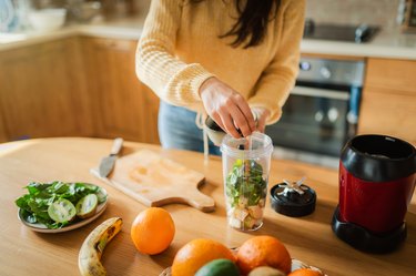 Person making smoothie with oranges and greens on kitchen counter