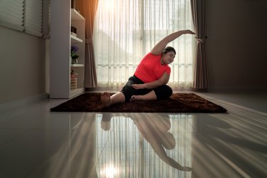 Woman exercising yoga Seated side bend pose alone on the floor in house, yoga meditation exercise at home. Take care of health concept.