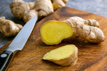 Close up of ginger roots, a piece cut, on wooden cutting board