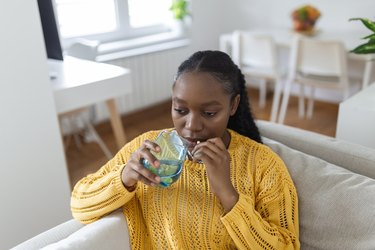 Woman sitting on couch and taking a white pill with a glass of water