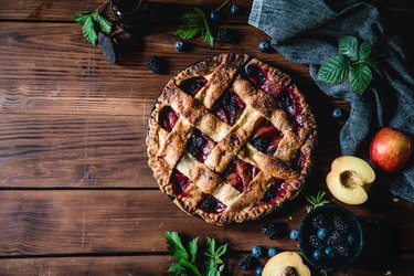 High angle photograph of a lattice fruit pie  with flaky pie crust next to fresh apples and cinnamon