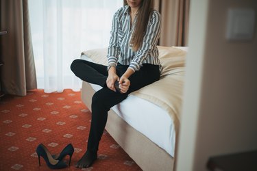 woman sitting on a bed massaging her foot and taking off her uncomfortable shoes, as a home remedy for bunions