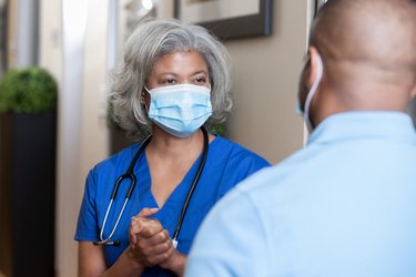 woman doctor discussing cholesterol levels with male patient wearing face masks