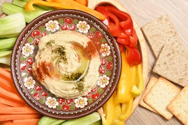 A plate of hummus with olive oil, spices and vegetables.