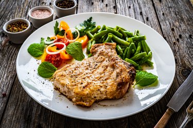 grilled 2-inch pork chop with boiled green bean and fresh vegetable salad on wooden table