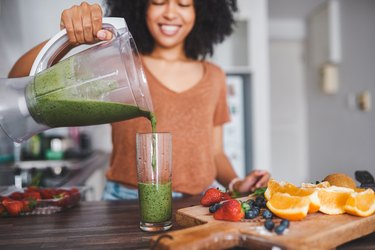 Woman blending a green smoothie for skin health with ingredients like spinach and bananas.