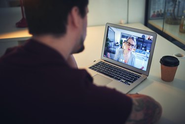 A man sits at a desk while video chatting with a woman through a laptop