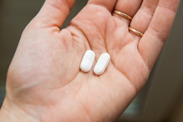 Close-up view of a hand holding two white pills of mangesnium and manganesein the palm