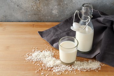 Vegan coconut milk and flakes on a dark gray napkin and a wooden table, animal friendly alternative to dairy products, copy space, selected focus