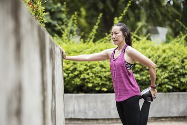 Runner in pink tank top and long leggings performing best leg stretch using a wall for extra balance.