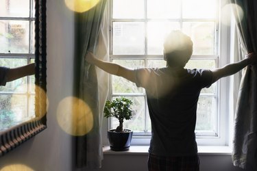 A man opening the curtains in the morning to get sunlight, so he can get better sleep at night