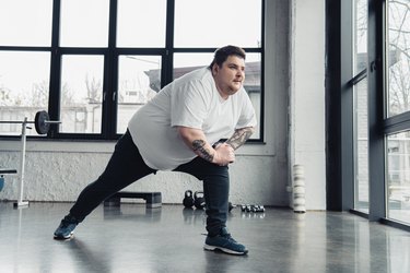 overweight tattooed man stretching legs at sports center