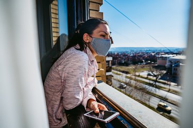 Woman in a mask checking the window to see if the room is well ventilated