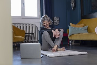 smiling senior woman watching on laptop while sitting at home, trying exercises for getting up from the floor