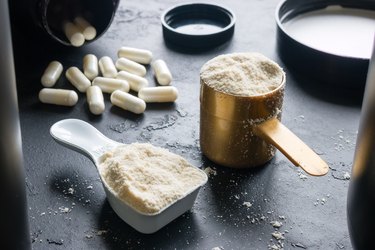 measuring cups filled with powdered supplements next to white capsules on a black counter
