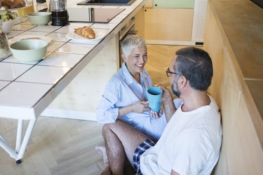 mature caucasian man and woman sitting on the floor drinking from mugs