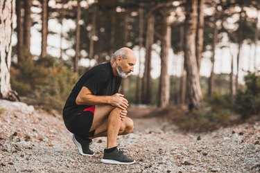 Man experiencing knee pain while running outdoors in the forest