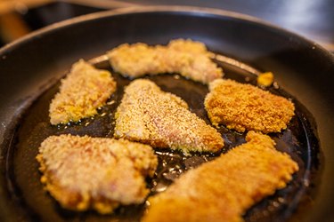 close up of breaded chicken frying in oil in a black skillet