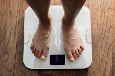 Top down view of feet standing on white digital bathroom scale over wooden floor