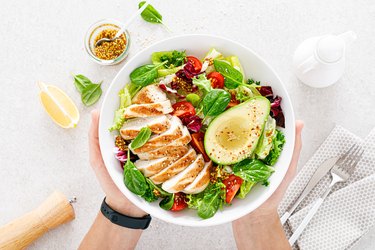 A Plate to Help You Get More Protein With Grilled Chicken and Fresh Vegetable Salad of tomato, avocado, lettuce and spinach. Healthy and detox food concept. Ketogenic diet. Buddha bowl in hands on white background, top view