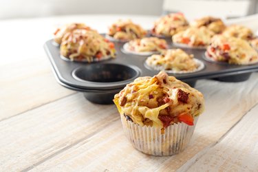 Tasty baked pizza muffins in a pan with one on the table