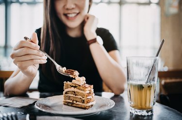 美丽的微笑的年轻的亚洲女人有蛋糕和冰茶放松和享受的时刻下午在咖啡厅