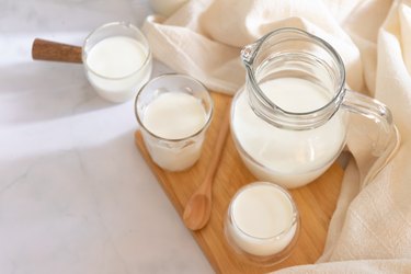 Milk, one of the 9 major food allergens,  in clear jars and glass of milk on wooden board. Healthy drink concept.