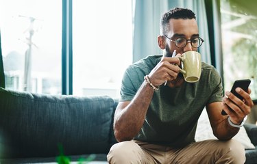 A man sitting on the couch drinking coffee and checking the pollen forecast, as a natural remedy for allergies