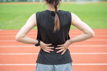 Back view of young runner suffering from back pain when running