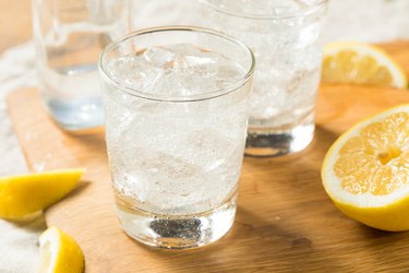 Close view of glasses of carbonated water with ice on a wooden board, surrounded by lemon slices to represent the benefits of carbonated water
