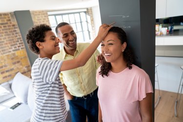 Smiling family measuring their mother's height against the wall