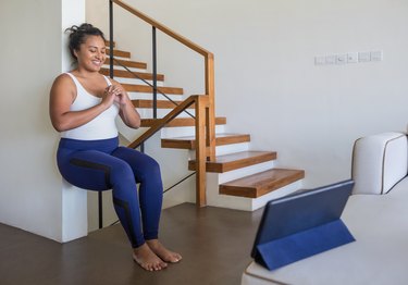 Smiling person with a ponytail doing a wall sit during her at-home workout with an iPad