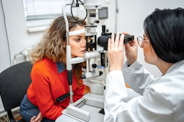 A close up of a person in a red long sleeve shirt sitting with the eye doctor for an exam.