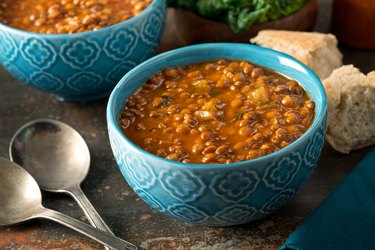 Curried oxalate-rich Lentil Soup in blue bowl on table with spoons and bread