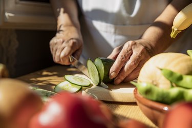 Senior woman cutting low-oxalate cucumber in kitchen