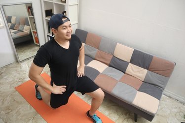 Asian man doing exercise at home while watching online video instruction on laptop, indoor home workout, keep healthy on new normal lifestyle, squat lunges