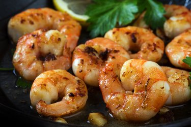 vitamin E-rich prawns shrimps roasted in a black pan with garlic, lemon and italian parsley garnish, close up