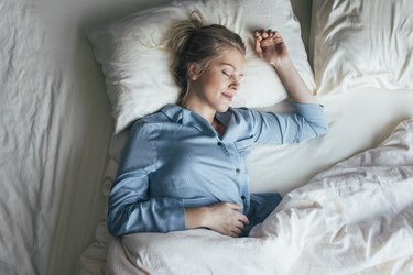 Overhead shot of a woman in blue pajamas sleeping on her left side in a bed with white sheets and blankets