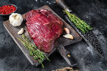 Venison raw deer meat on a cuuting board with herbs. Black background. Top view