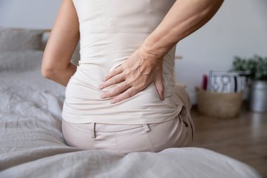 Older person sitting on bed and holding lower back because of sciatic pain